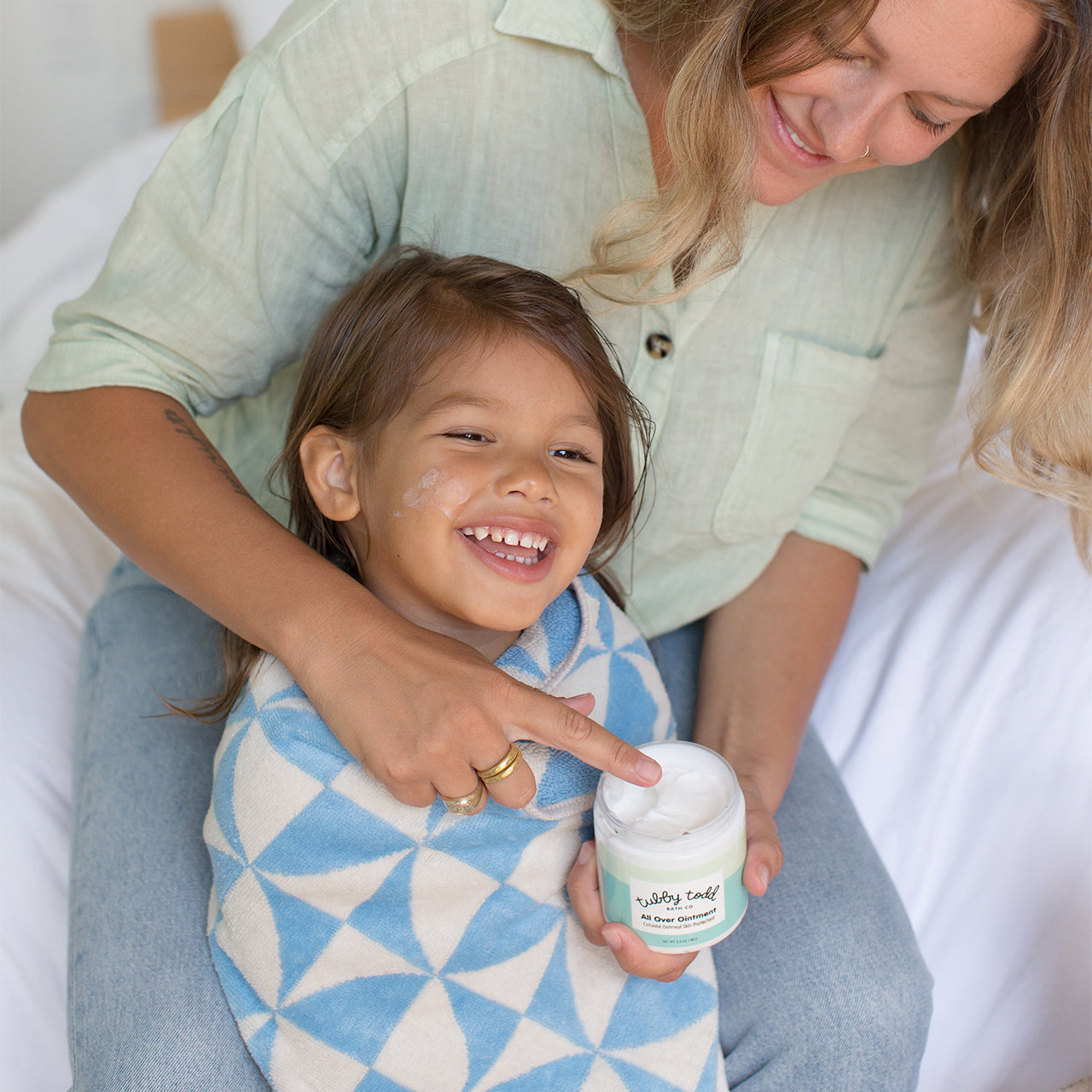 Mama applying OTC All Over Ointment on her daughter who is wrapped in a towel